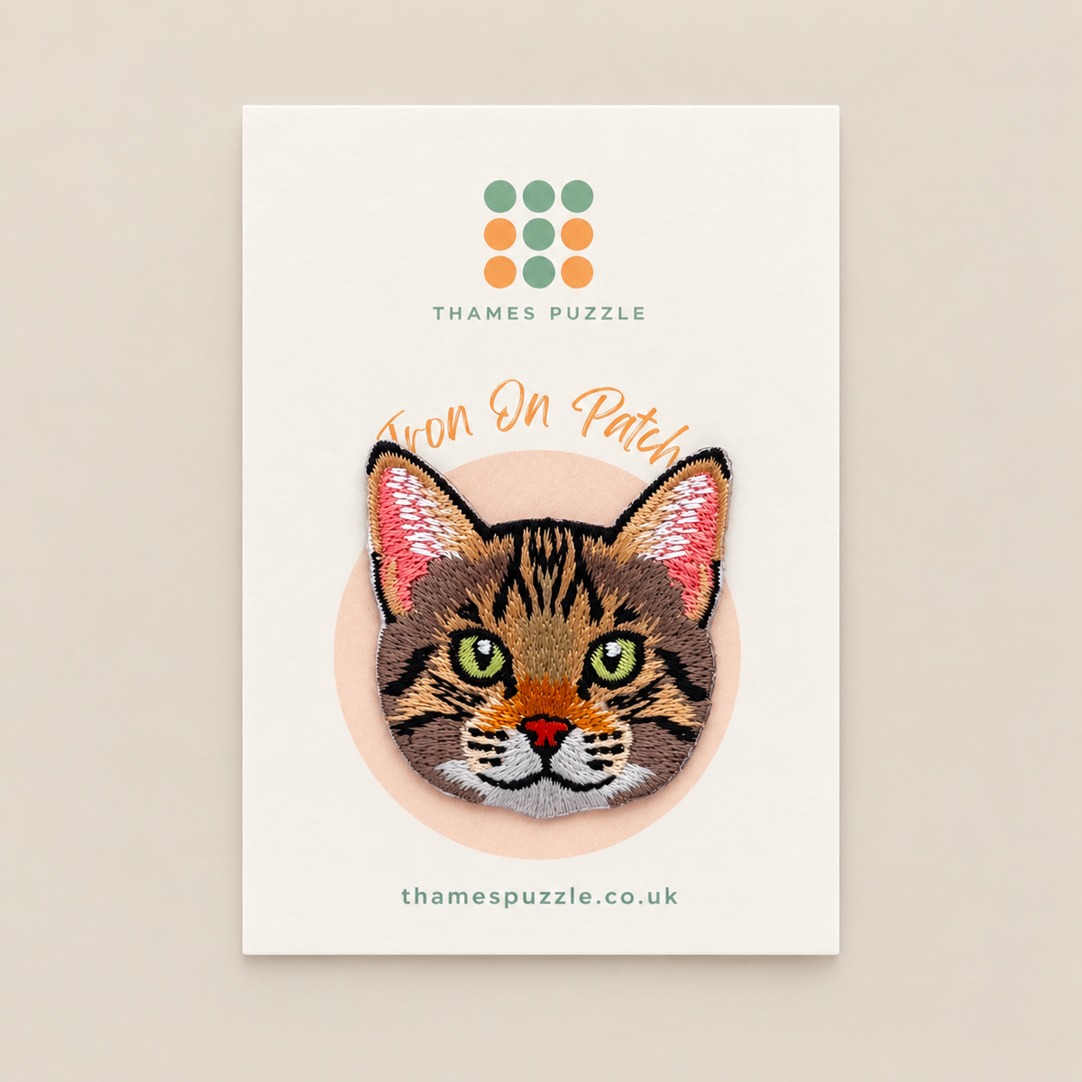 An embroidered cat patch displayed on its branded backing card. The patch features a tabby cat's face with green eyes, pink inner ears, and a small orange nose.