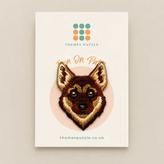 A product card for 'Iron On Patch' by Thames Puzzle, featuring a detailed embroidered German Shepherd dog head patch on a cream background with the brand logo and website.
