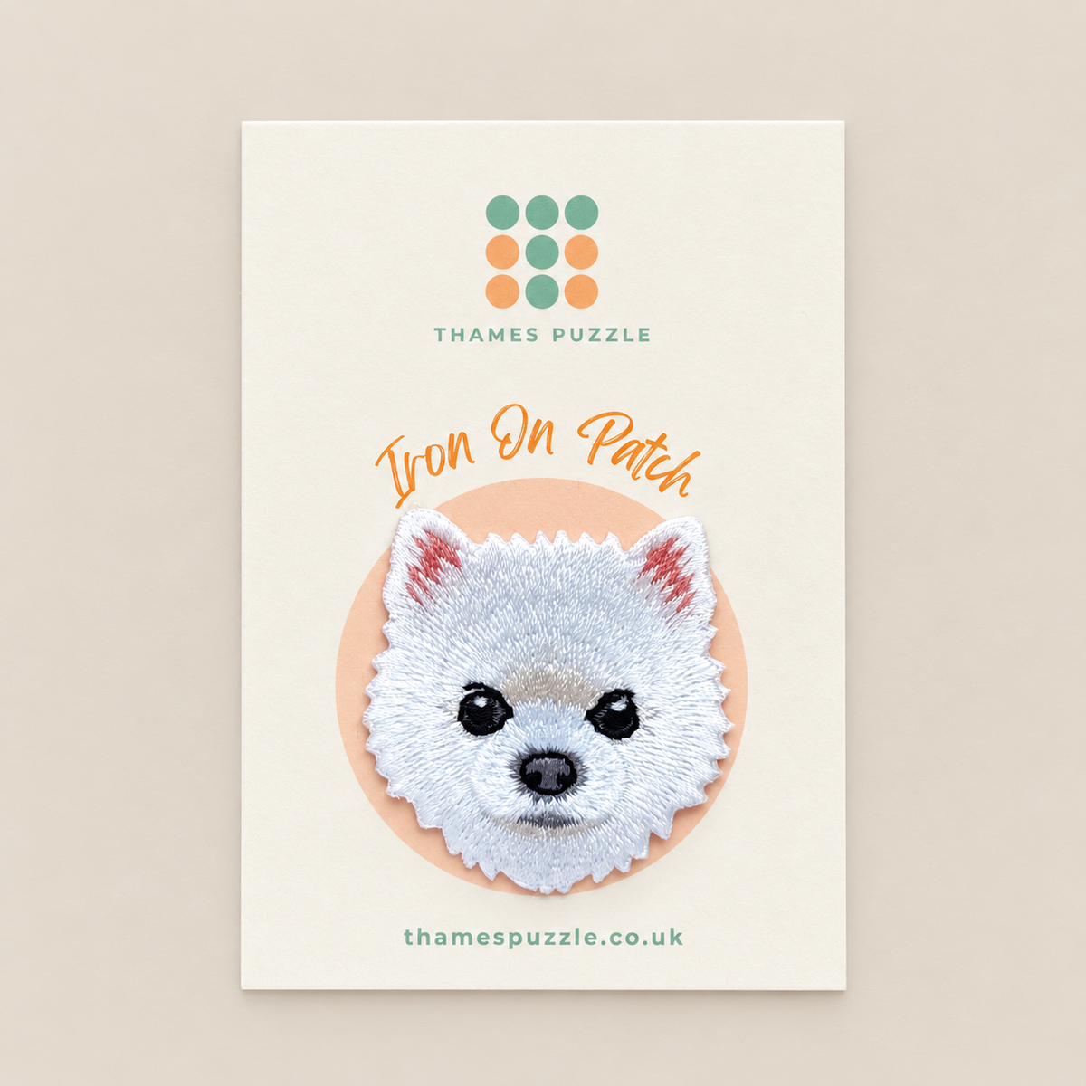 An embroidered dog face iron-on patch by Thames Puzzle, displayed on its cream-colored backing card. The patch features a white dog head with pink inner ears, black eyes and nose, and is set against a peach circular background.