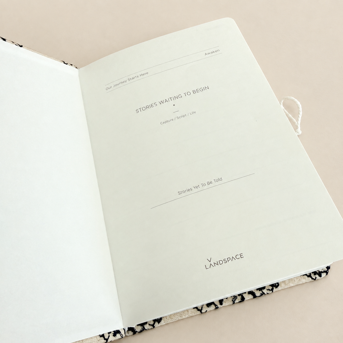 An open notebook or journal on a light beige background, showing blank white pages with printed text and a black-and-white patterned cover edge visible at the bottom.