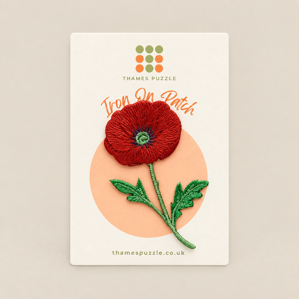 An embroidered iron-on patch of a red poppy flower with green leaves and stem, displayed on its white backing card from Thames Puzzle.