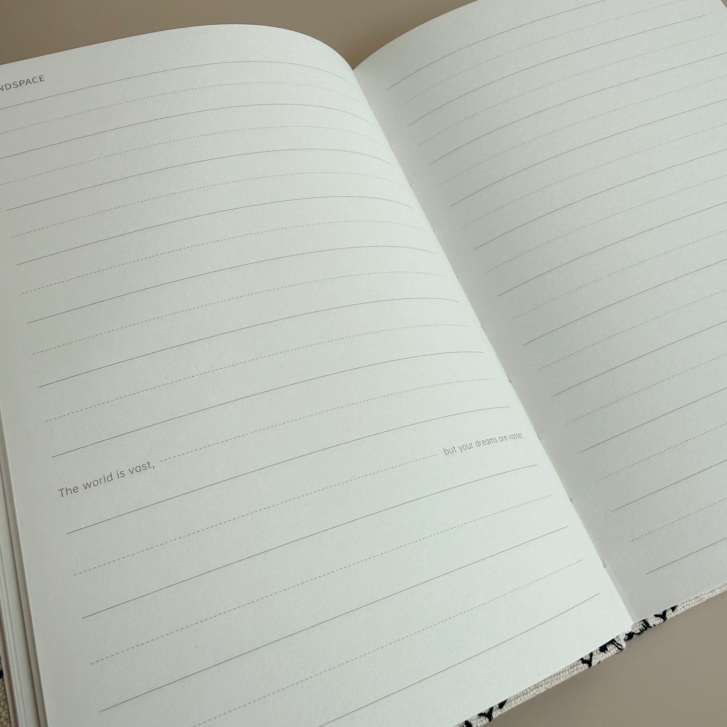 An open lined notebook with blank writing pages, photographed at an angle against a neutral beige background.