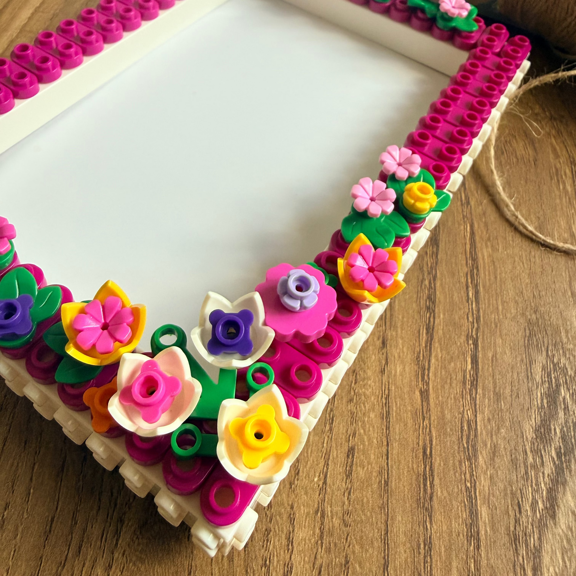 A rectangular picture frame decorated with colorful plastic building-block flowers and green leaves around the border, placed on a wooden tabletop.