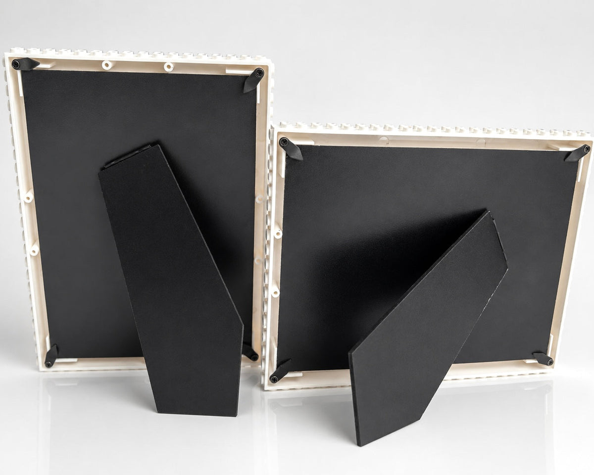 Two black picture frames shown from the back on a light gray studio background, with one frame leaning against the other.